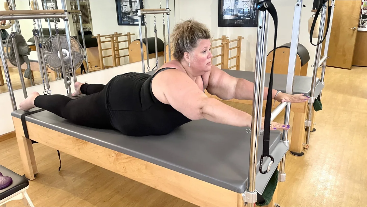 A client reaches forward using the push-through bar on a Pilates tower in Lakewood