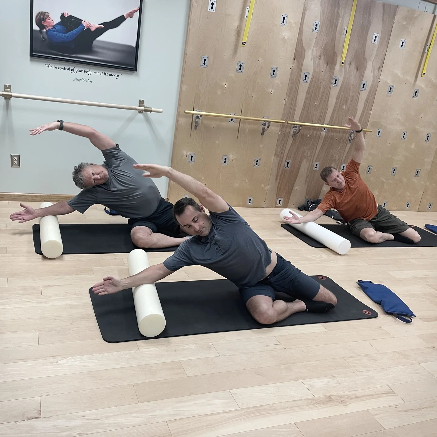 Clients practice side-lying movement with foam rollers in a Lakewood mat class
